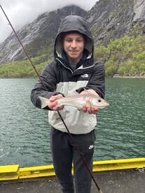 Young angler proudly displaying a freshly caught fish while fishing in a scenic fjord environment.