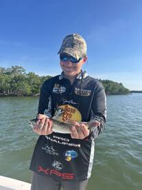 A young angler proudly displaying a beautiful Speckled Trout while fishing in a scenic coastal environment.