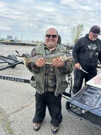 Angler proudly displaying a Walleye caught during a fishing trip, with a boat and fellow anglers in the background.