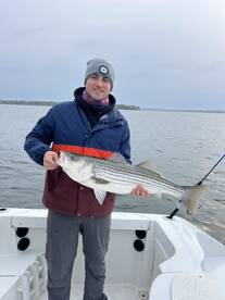 Angler proudly displaying a large Striped Bass while fishing on a boat, showcasing a successful day on the water.