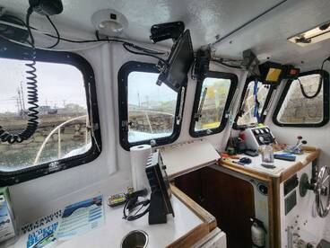 Interior view of a fishing boat's helm, showcasing electronics and controls, with a rainy atmosphere visible through the windows.