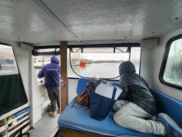 Interior view of a fishing boat showing two individuals preparing for a fishing trip, with a focus on the seating area and helm.