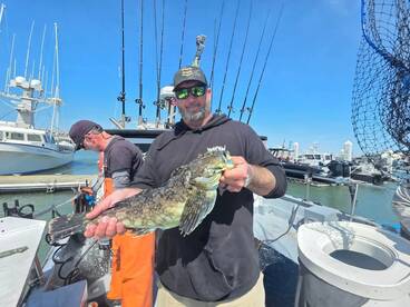 Angler proudly displaying a large fish on a boat, with fishing gear and other boats visible in the background.