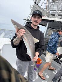Angler proudly displaying a caught shark on a fishing charter, showcasing a successful day at sea.