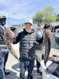 A happy angler proudly displaying two large Halibut caught during a fishing trip, surrounded by fellow anglers at the dock.