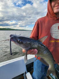 A young angler proudly displaying a Catfish while fishing on a scenic lake, showcasing a beautiful day on the water.