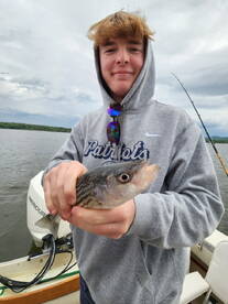 A young angler proudly displaying a striped bass while fishing on a calm lake, showcasing a relaxed day on the water.