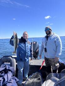 Two anglers proudly displaying a large Walleye while fishing on a sunny day in a boat.