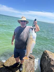 Angler proudly displaying a large Redfish caught while fishing off the rocks in a coastal environment.
