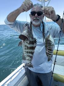 An angler proudly displaying two large Grouper caught while fishing offshore, showcasing the excitement of a successful day on the water.