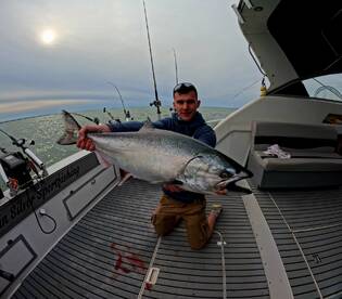 Angler proudly displaying a large Salmon on a fishing charter in open waters, showcasing the thrill of sport fishing.