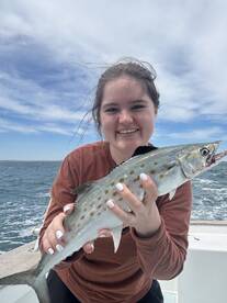 A young angler proudly displaying a Spanish Mackerel while fishing on a boat, showcasing a beautiful day on the water.