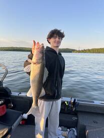 A young angler proudly displaying a large Walleye while fishing on a calm lake, showcasing a successful catch.