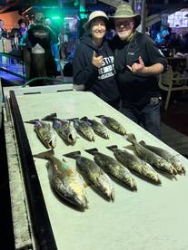 A group of anglers proudly displaying their catch of speckled trout on a board at a lively fishing venue.