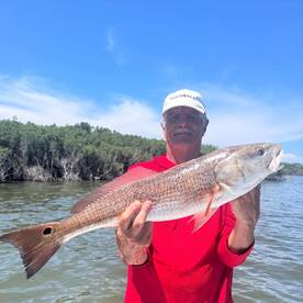 An angler proudly displaying a large Redfish while fishing in a scenic coastal environment.