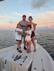 A family proudly displaying their catch of Speckled Trout on a boat during a sunset fishing trip.