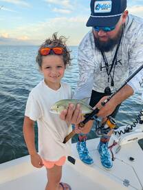 A young angler proudly displaying a small fish while fishing on a boat, enjoying a family outing on the water.