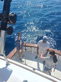 A group of anglers on a boat enjoying a fishing trip, with one person proudly displaying a freshly caught fish against a sparkling blue ocean backdrop.