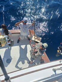 Two anglers actively fishing on a boat, with one holding a freshly caught fish while the other prepares to reel in. The vibrant blue water adds to the excitement of the fishing experience.