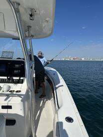 Angler casting a line from a center console boat while enjoying a sunny day on the water, with a city skyline in the background.