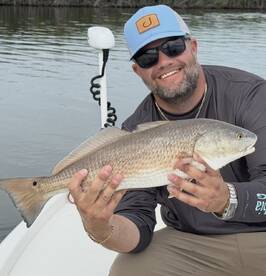 Angler proudly displaying a large Redfish while fishing from a boat in a scenic waterway.