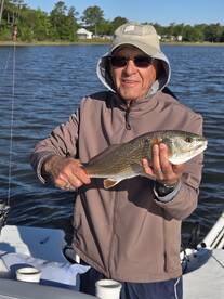 An angler proudly displaying a Redfish while fishing on a calm river, showcasing a successful catch during a serene morning outing.