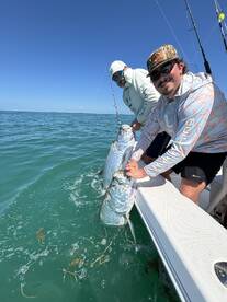 Two anglers proudly displaying their catch of Tarpon while fishing in clear waters, showcasing a successful day on the boat.