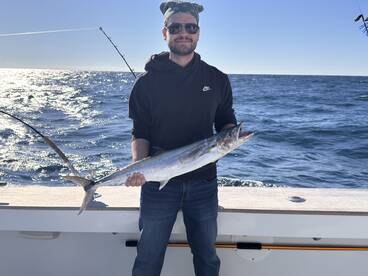Angler proudly displaying a large King Mackerel while fishing offshore, showcasing a successful day on the water.