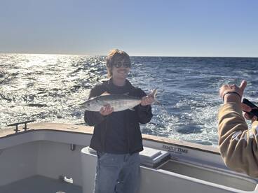 A young angler proudly displaying a fish on a boat during a fishing trip, with the ocean shimmering in the background.