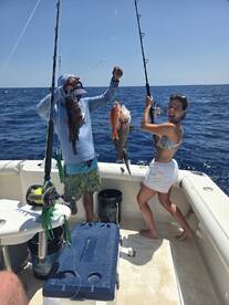 Two anglers celebrating their catch of colorful fish, including a Snapper, while fishing on a sunny day in open waters.