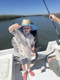 A young angler proudly displaying a caught fish while fishing on a boat in a scenic waterway.
