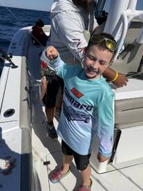 A young angler proudly holding a small fish while fishing on a boat, enjoying a day out at sea.
