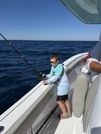 A young angler is actively fishing from a boat, showcasing the excitement of deep-sea fishing in clear blue waters.