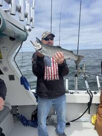 Angler proudly displaying a large trout while fishing on a charter boat, showcasing a successful day on the water.