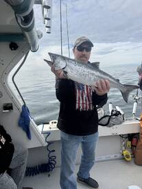 Angler proudly displaying a large salmon while fishing on a boat, showcasing a successful day on the water.