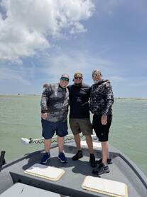Three anglers posing together on the bow of a fishing boat, enjoying a sunny day on the water.