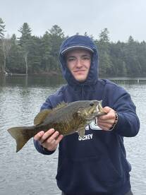 A young angler proudly displaying a large Smallmouth Bass while fishing on a calm lake surrounded by trees.