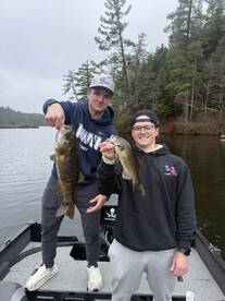 Two anglers proudly displaying their catch of smallmouth bass while fishing from a boat in a scenic lake.