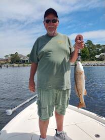 An angler proudly displaying a Redfish while standing on the boat, enjoying a sunny day on the water.
