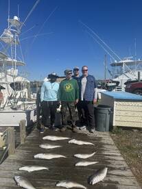 A group of four anglers proudly posing with their catch of multiple fish laid out on the dock after a successful fishing trip.