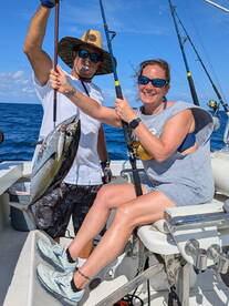 Two anglers proudly displaying a large Tuna while fishing on a boat in open waters.