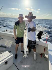 A young angler and an adult proudly display a large Barracuda on a fishing boat, enjoying a successful day on the water.