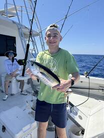 A young angler proudly displaying a caught fish aboard a fishing charter in open waters.