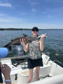 A happy angler proudly displaying a large catfish while fishing on a sunny day, surrounded by family on a boat.