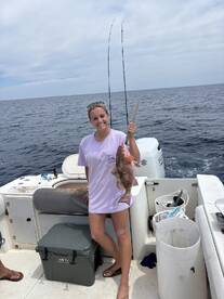 A young woman proudly displaying a caught Red Snapper while fishing on a boat in open waters.