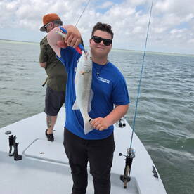A young angler proudly displaying a caught Redfish while fishing on a boat in coastal waters.