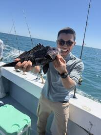 Angler joyfully displaying a Black Sea Bass while fishing on a sunny day, showcasing the excitement of a successful catch.