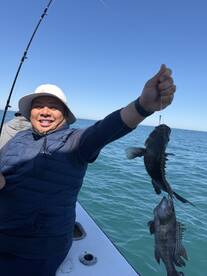 Angler proudly displaying two Black Sea Bass while fishing on a boat in clear blue waters.