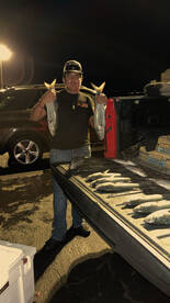 A young angler proudly displaying two large fish after a successful night fishing trip, with several more fish laid out in the truck bed.