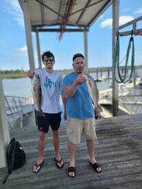 Two anglers proudly displaying their catches of striped bass on the dock, showcasing a successful fishing trip.